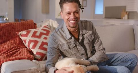 Young man smiling and cuddling light-colored puppy while relaxing on cozy modern living room sofa