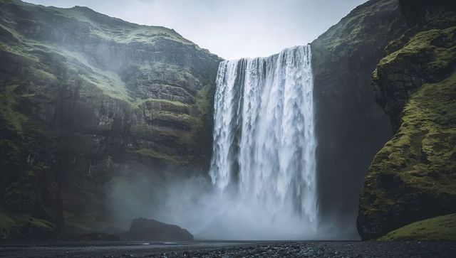 Moss-covered cliffs with plunging waterfall creating mist-filled canyon under overcast sky