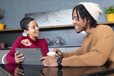 African american couple chatting over tablet and coffee in modern cafe, smiling connection