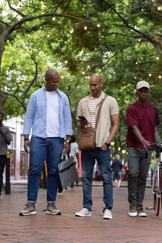 African american men walking under string lights on tree-lined urban street checking smartphone