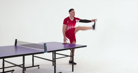 Energetic athlete practicing high kick near ping-pong table