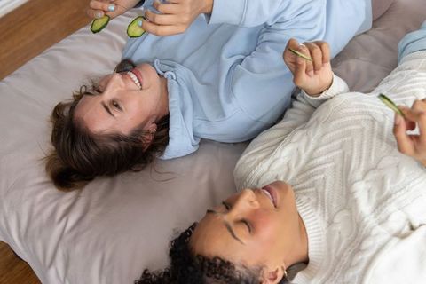 Multiracial friends lounging and playing with cucumber slices on cozy neutral-toned mattress
