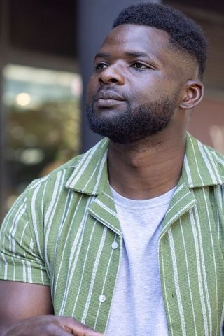 African american man sitting at cafe looking thoughtful in green striped shirt