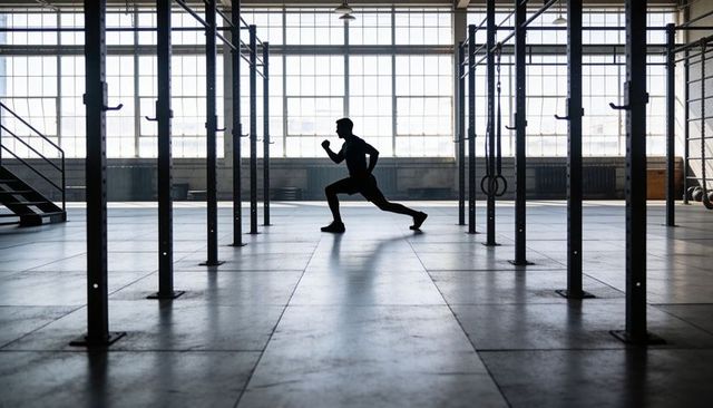 Silhouette athlete lunging in industrial gym rig backlit minimalist workout training scene