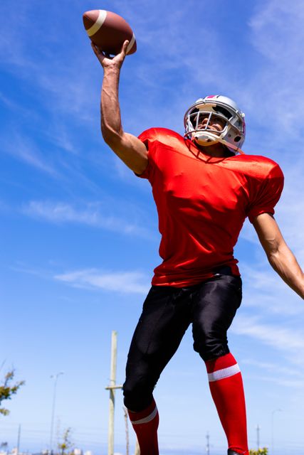 Low angle view of an African American football player catching a ball during a game on a sunny day. Ideal for use in sports-related content, athletic promotions, fitness campaigns, and teamwork illustrations.