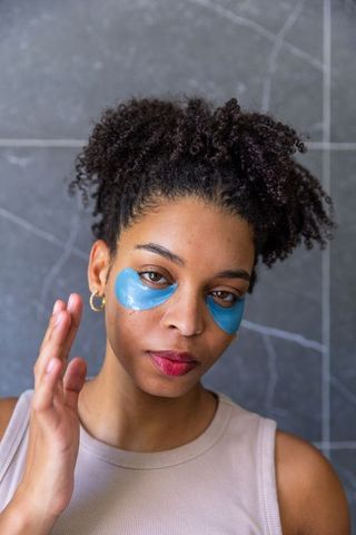 African american woman wearing blue under-eye hydrogel patches curly hair skincare portrait