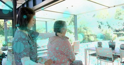 Caregiver comforting senior woman on sunlit patio with garden view and gentle touch