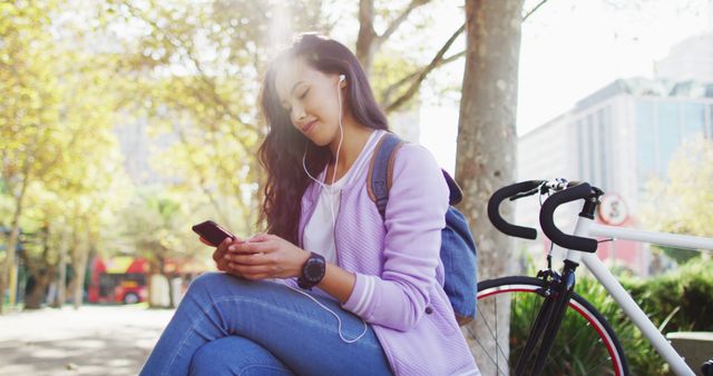 Asian woman wearing earphones using smartphone sitting in the park. modern lifestyle and living concept