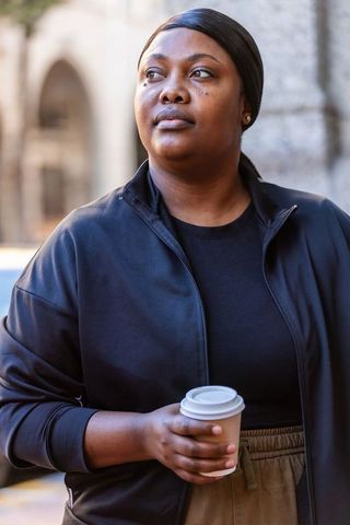 African american woman standing on city sidewalk holding coffee cup looking confident