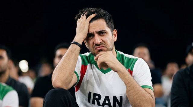 Nervous iranian football fan holding head, resting elbow on knee in stadium at night