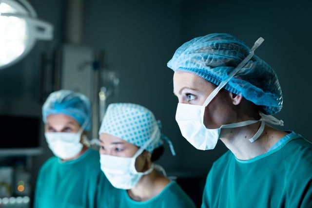Three diverse female surgeons in face masks concentrating during surgery in operating theatre. Medical services, hospital and healthcare concept.