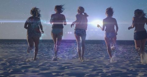 Friends running toward ocean at golden hour on sandy beach leaving footprints, lens flare