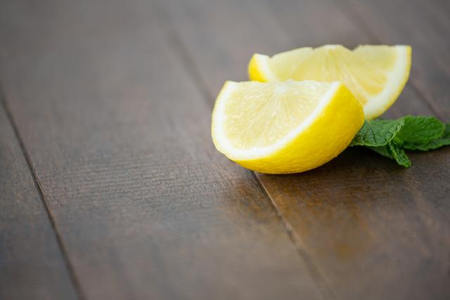 Close-up of lemon wedges and mint leaves on a wooden board. Ideal for use in food blogs, recipe websites, cooking magazines, and health-related content. Perfect for illustrating fresh ingredients, summer recipes, and natural food concepts.
