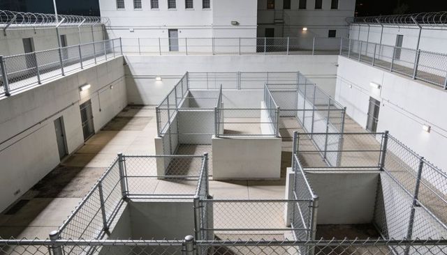 Nighttime prison exercise yard featuring fenced individual enclosures and perimeter walkways