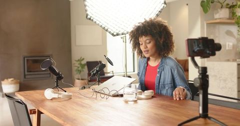 Young african american woman recording podcast at home studio with softbox and camera