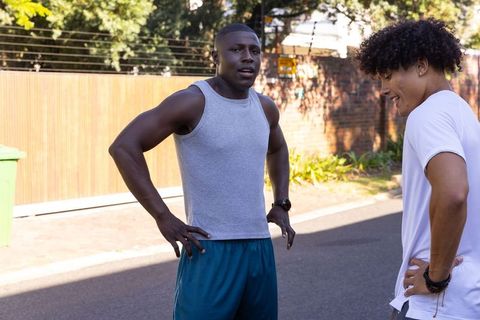 Diverse male friends catching breath after outdoor run on suburban street chatting