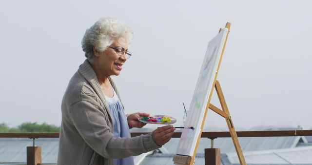 Senior woman painting outdoors, illustrating a joyful moment of creative expression in retirement. Useful for content about healthy aging, hobbies for the elderly, and the benefits of creative activities. Ideal for marketing materials, educational resources, and lifestyle articles.