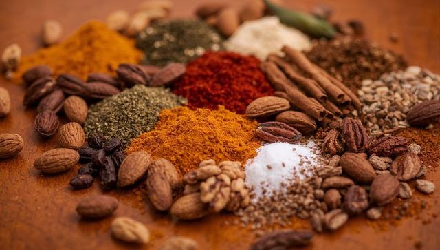 Colorful Ground Spices and Whole Nuts on Warm Wooden Tabletop with Cinnamon and Cardamom
