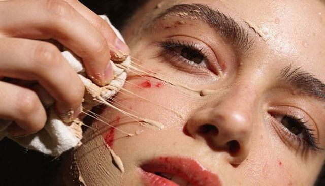 Peeling prosthetic makeup revealing fake blood on young woman's face closeup special effects