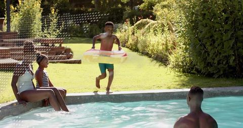 Joyful family playing at backyard pool with child running carrying inflatable swim ring