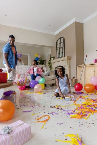 African american family tidying living room after party, child sweeping confetti cleanup