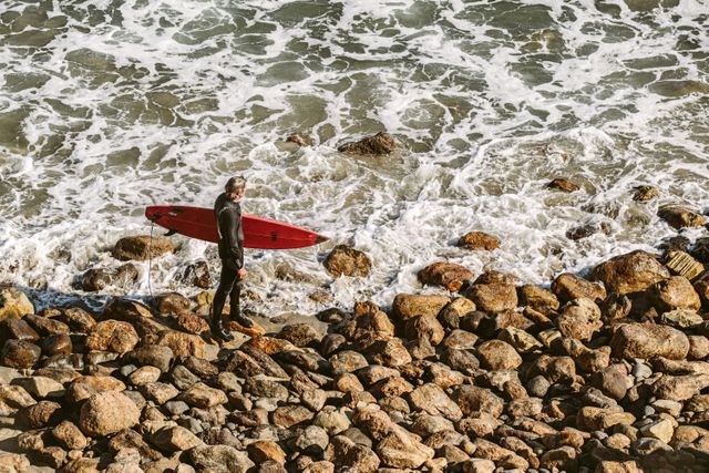 Man Wearing Wetsuit and Holding Red Surfboard on Shore - Download Free Stock Photos Pikwizard.com