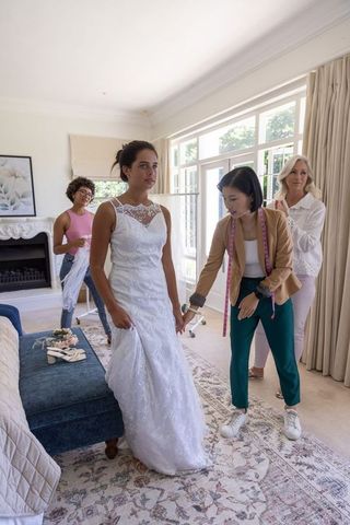 Bridal home fitting with asian fitter measuring hem, bride wearing lace wedding gown