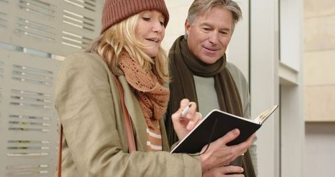Mature couple planning trip in lobby, woman writing notes while partner holds notebook