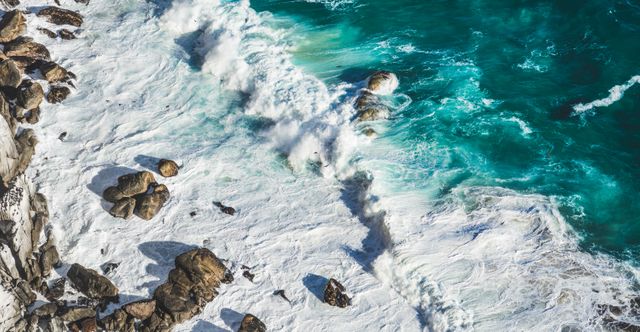 Aerial view of powerful waves crashing on rocky coastline with turquoise waters. Dynamic surf and natural beauty perfect for travel blogs, nature websites, or ocean conservation campaigns. Great for illustrating raw natural scenes, rugged coastlines, and maritime subject matter.