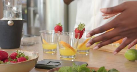 Hands arranging citrus cocktail glasses with strawberries on wooden kitchen counter