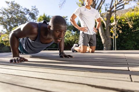Diverse male training partners doing push-ups on wooden deck with fitness trackers