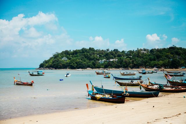 Traditional wooden fishing boats anchored along a serene tropical beach under clear blue skies. Calm sea and abundant greenery in the background. Ideal for promoting travel destinations, vacation spots, tropical getaways, and outdoor activities.