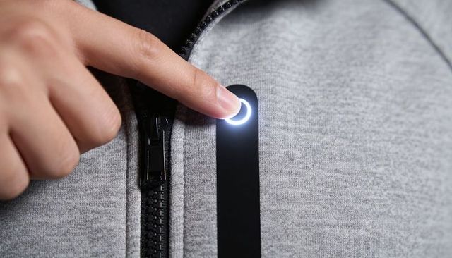Pressing finger activating led button on grey zip-up tech hoodie for smart wearable control