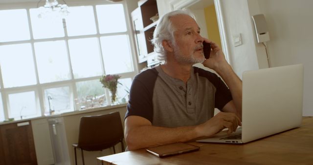 Senior Man Multitasking with Laptop and Phone in Modern Home Kitchen - Download Free Stock Images Pikwizard.com