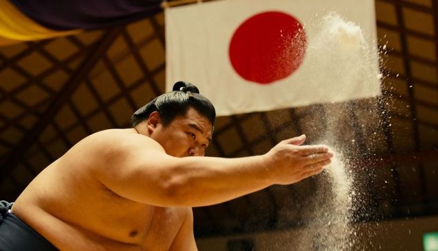 Japanese sumo wrestler performing salt ritual before match under national flag