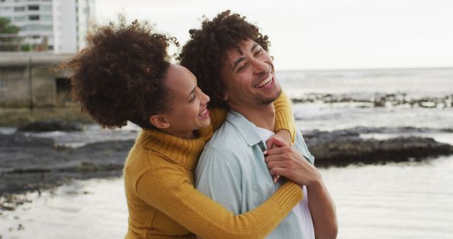 Couple embracing and laughing together at beachside, expressing joy and happiness. Perfect for advertisements on relationship advice, romantic getaway promotions, or lifestyle blogs focused on love and happiness.