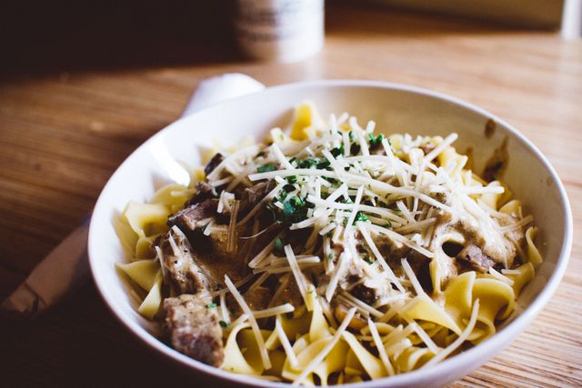 Beef stroganoff served in white bowl with egg noodles and garnished with Parmesan cheese and herbs. Perfect for food blogs, recipe books, and cooking magazines. Great to illustrate articles on comfort food, Italian cuisine, or home-cooked meals.