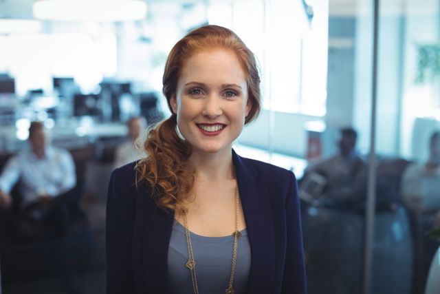 Businesswoman smiling confidently in a modern office environment. Ideal for use in corporate websites, business presentations, career-related articles, and promotional materials showcasing professional success and workplace culture.