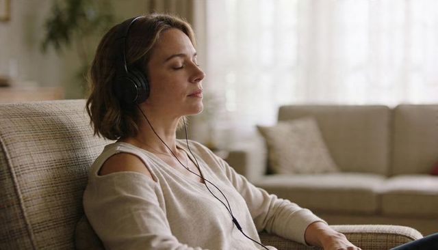Woman listening to music with headphones relaxing on sofa in sunlit neutral living room