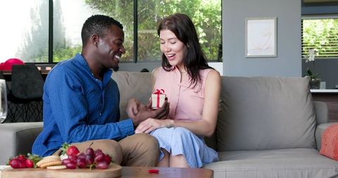 Interracial Couple Celebrating with Gift Exchange on Sofa