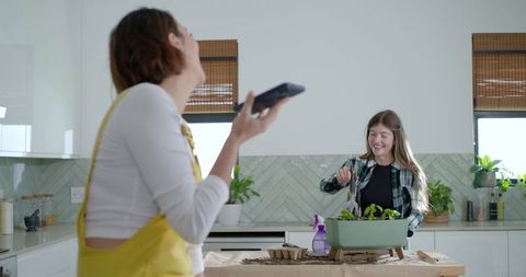 Friends laughing while planting indoor herb garden on kitchen counter