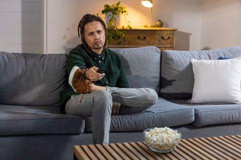 African american man relaxing on couch with remote and popcorn in cozy living room