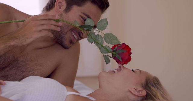 Couple expressing affection with a red rose while lying in bed. The intimate and romantic moment captures the delight and closeness shared, perfect for depicting romantic relationships, love, and intimate moments. Great for advertisements, Valentine's Day promotions, relationship blogs, and romantic greeting cards.