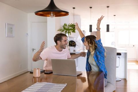 Excited Couple Celebrating Success at Home with Laptop