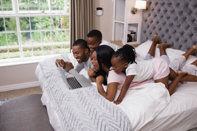 Family enjoying online shopping together on a cozy bed at home. Parents and children bonding over technology, creating a joyful and relaxed atmosphere. Ideal for use in advertisements for online shopping platforms, family-oriented products, or technology services.