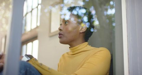 Woman in Yellow Sweater Talking on Phone By Window with Natural Light