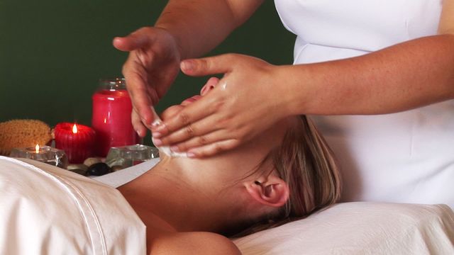 Professional massage therapist performing calming facial massage on woman in serene spa setting. Spa environment frequently booked by wellness brands, skin clinics, and beauty schools for promoting skincare tips and relaxation techniques. Ideal for advertising peaceful retreat experiences or skincare products.