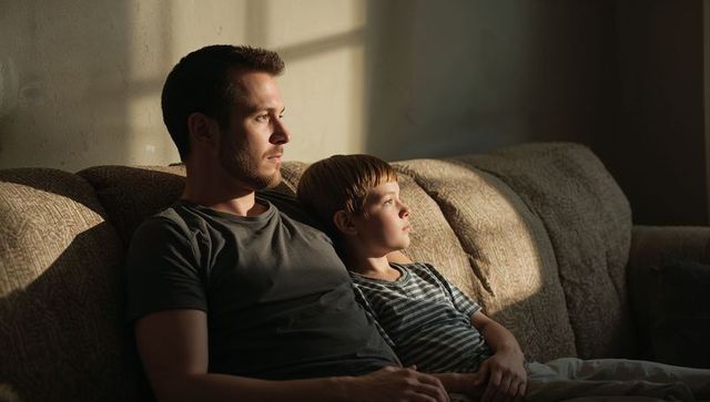 Father and son sharing quiet sunlit moment on couch, at home bonding during golden hour