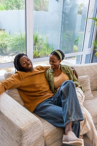 African american female couple reclining on sofa sharing intimate joyful moment at home