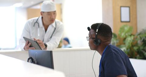 Black nurse wearing headset consulting with asian doctor at modern clinic reception desk